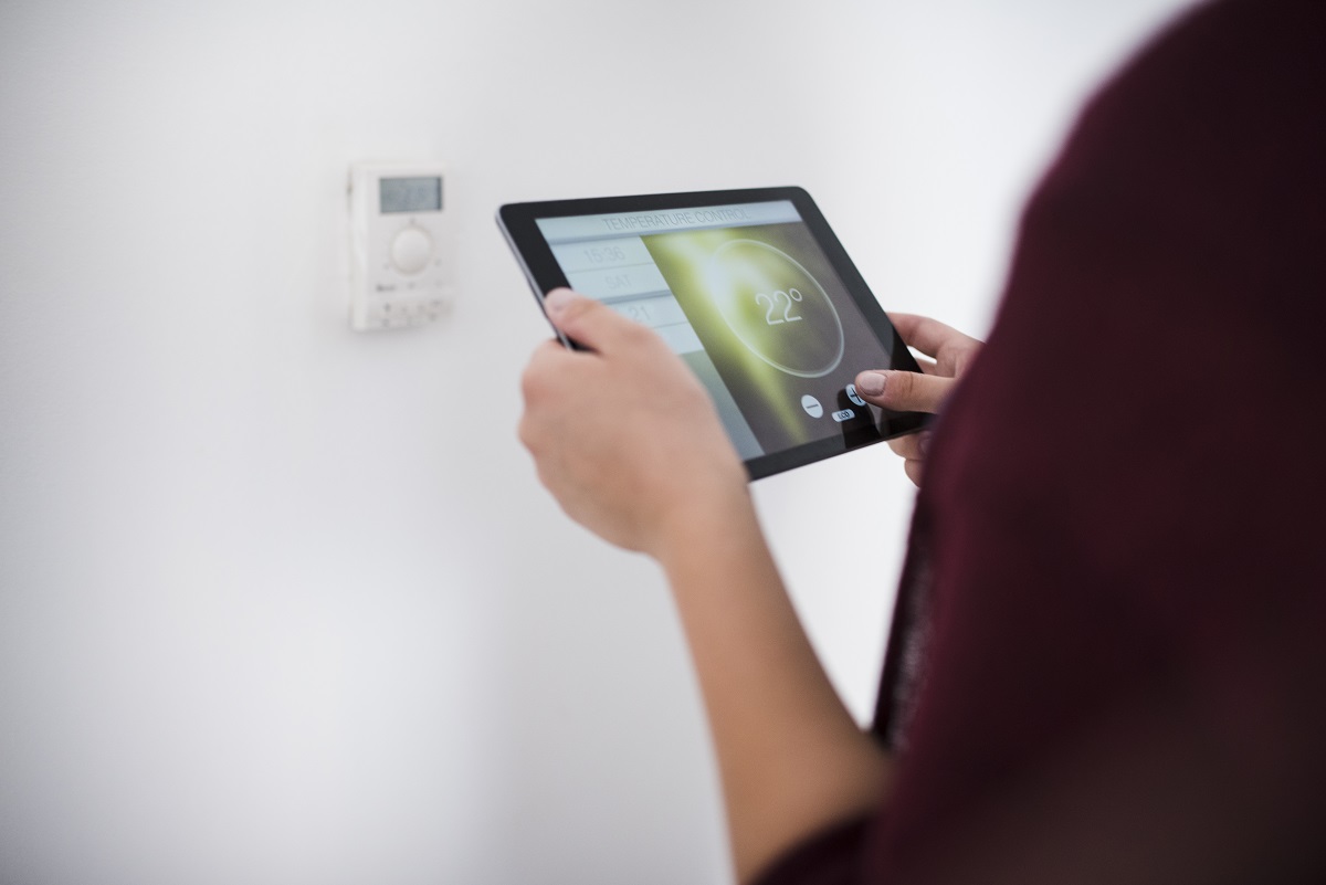 Young woman using digital tablet to adjust the temperature in the room